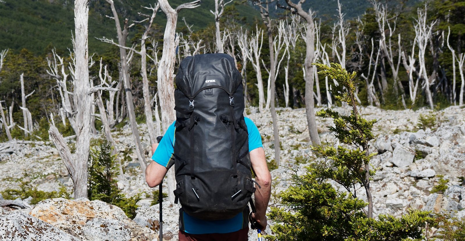 A mountaineer carrying a CRUX AK pack through alpine woodland